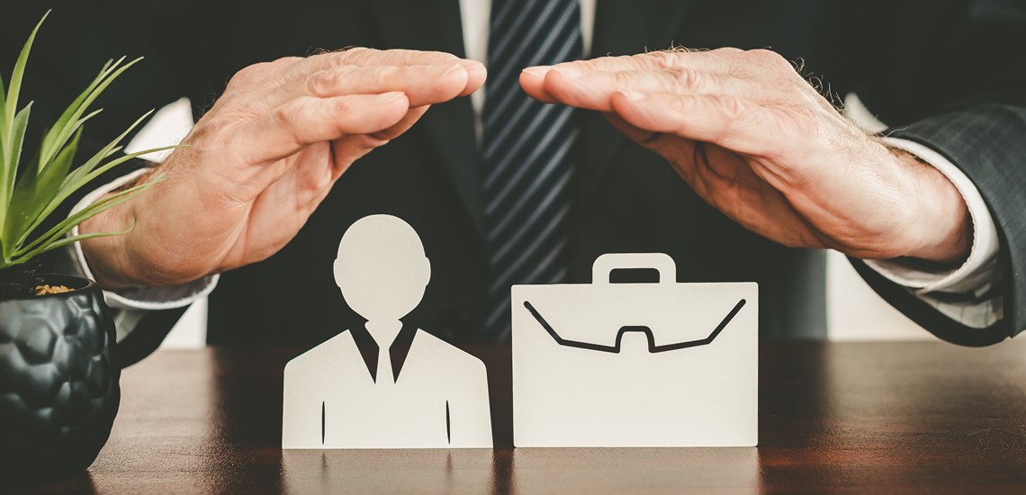 hands protecting miniature businessman and briefcase