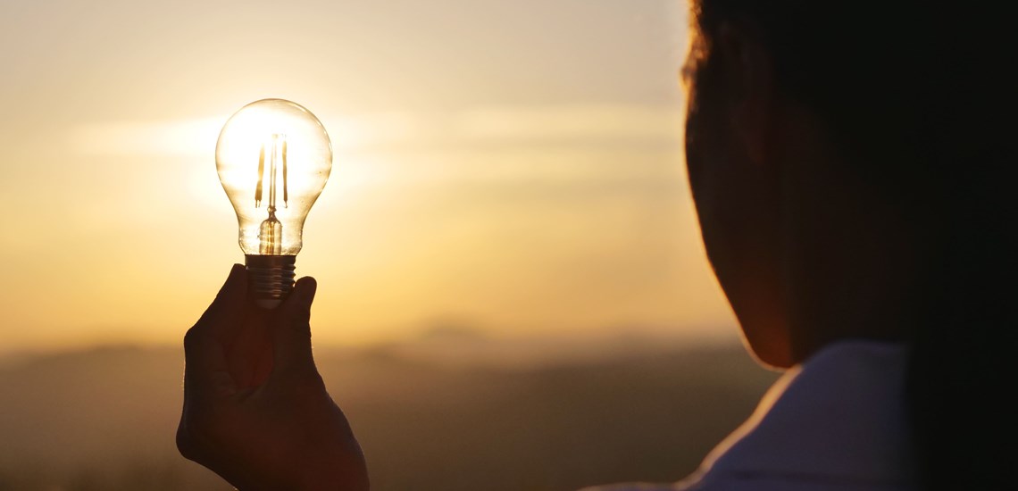 silhouette of a person holding a lightbulb sunset in horizon