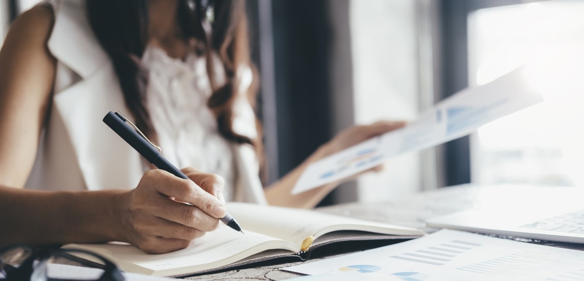 professional woman analysing data writing with pen at desk