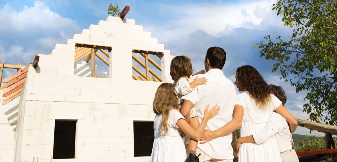 Family cuddling, looking up at their new build property being built.