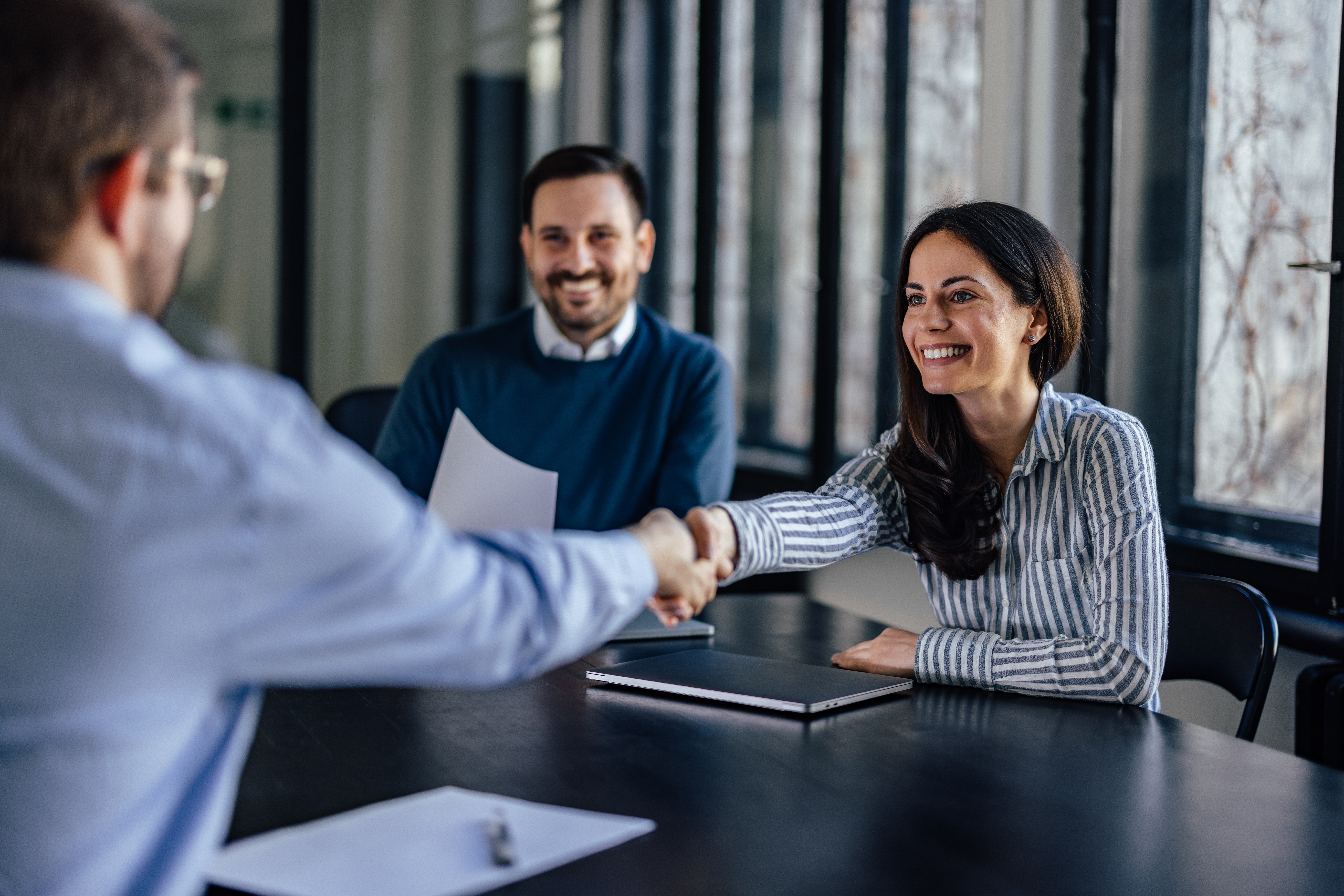 three people sitting around a table, two are shaking hands.
